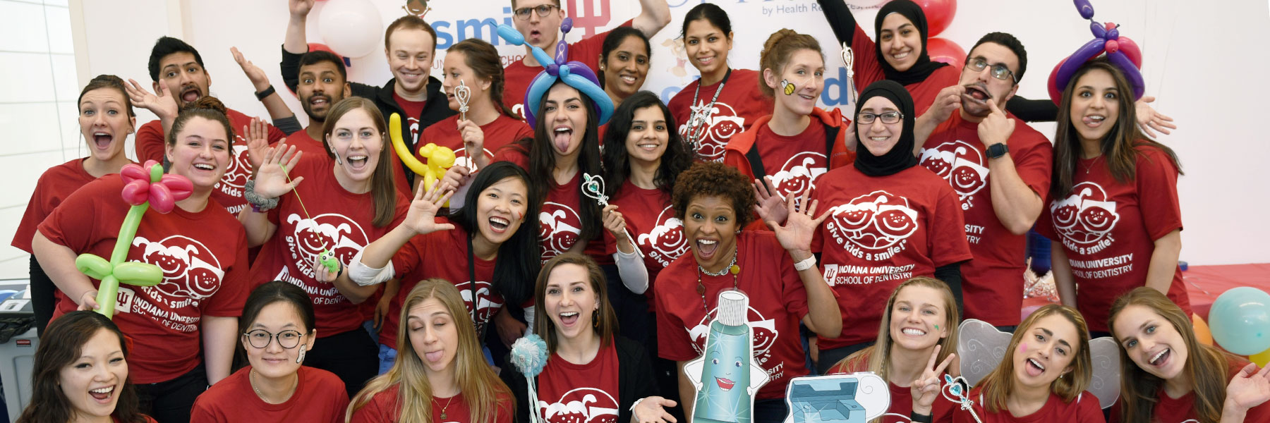 A group of dentistry students hold balloons and smile during a community outreach program.