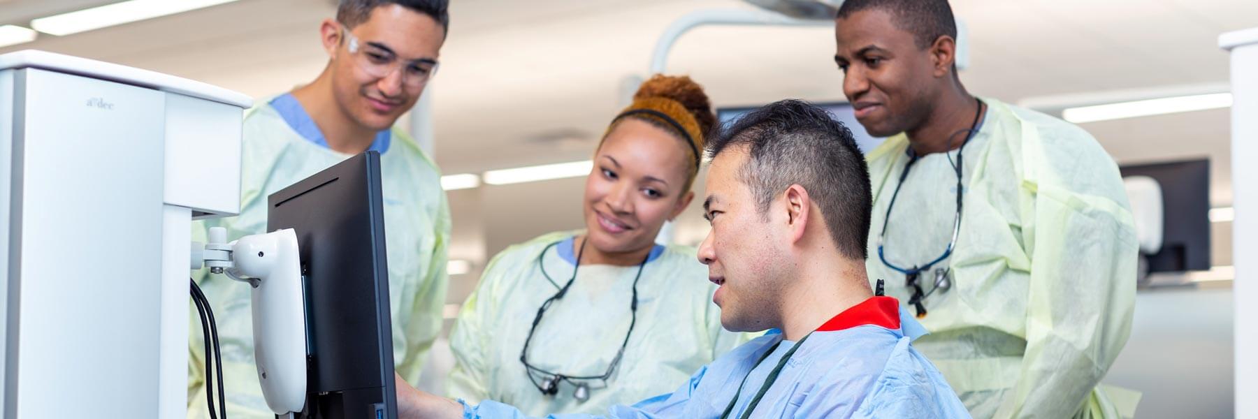 A man works with dental equipment and points to a monitor as other dentistry professionals observe.