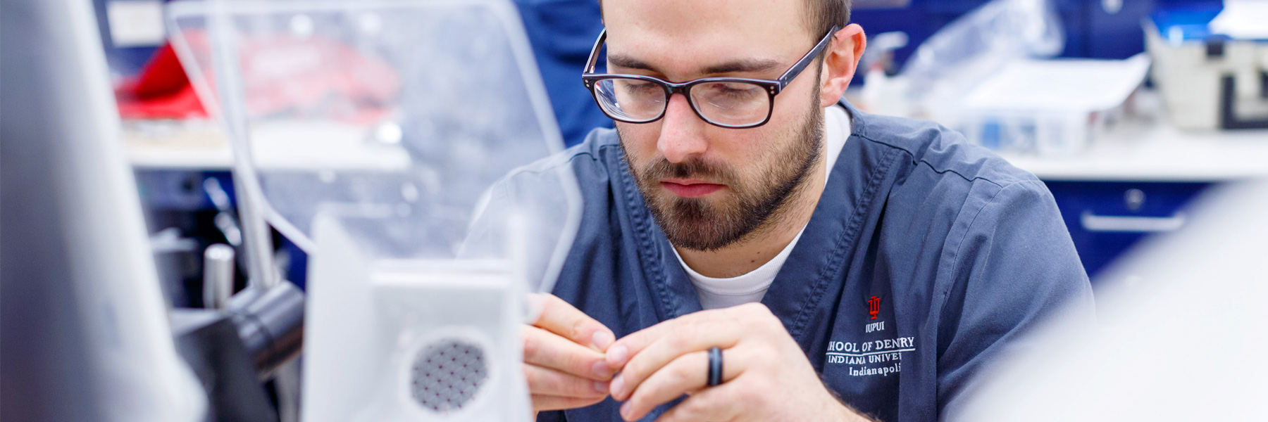 A dentistry student wears scrubs while he works in the lab.