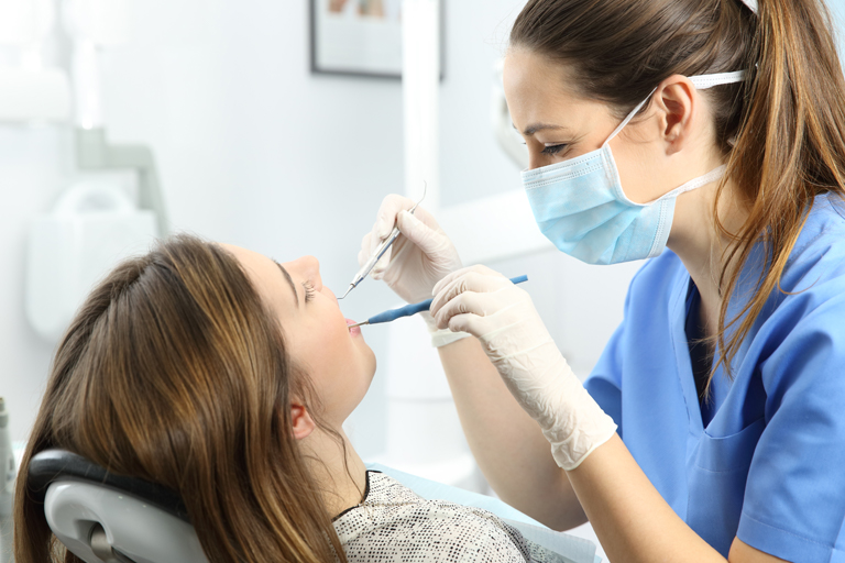 A dentistry professional works on a young girl's teeth with dental tools.